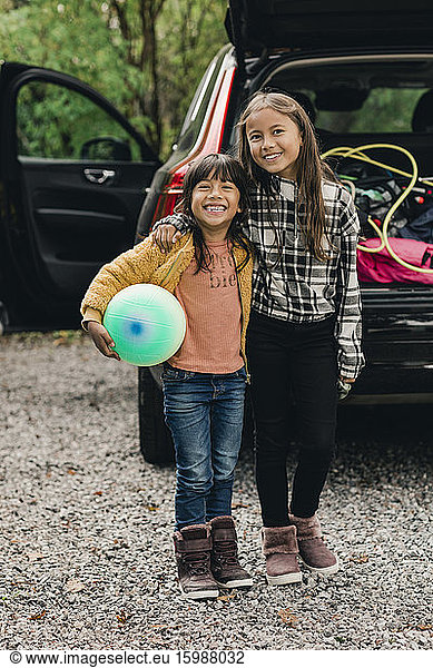 Portrait of smiling sisters standing against electric car