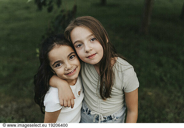 Portrait of smiling sisters standing with arm around at park