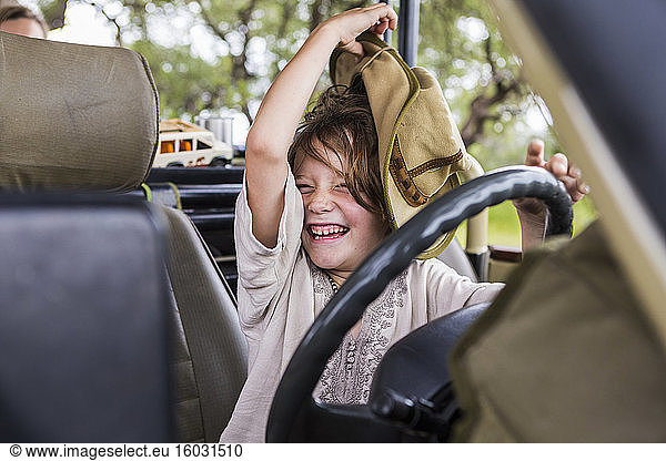 Portrait of smiling Six year old boy with a large hat in the driving seat of a safari vehicle