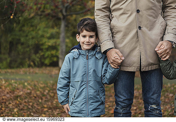 Portrait of smiling son holding hands with father while standing in park during autumn