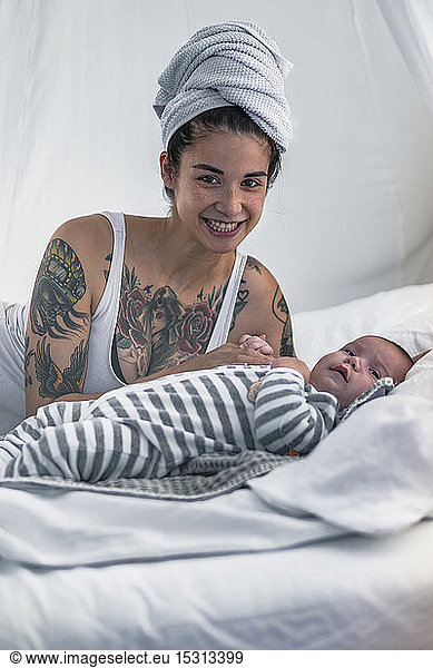 Portrait of smiling tattooed young woman with her baby in canopy bed