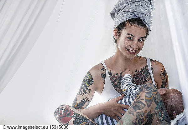 Portrait of smiling tattooed young woman with her baby in canopy bed