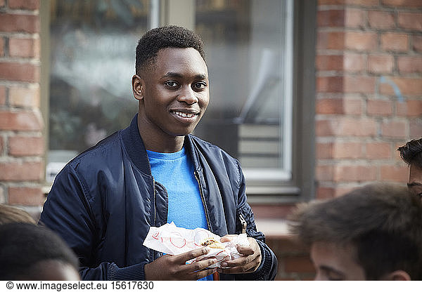 Portrait of smiling teenage boy holding food while standing outdoors