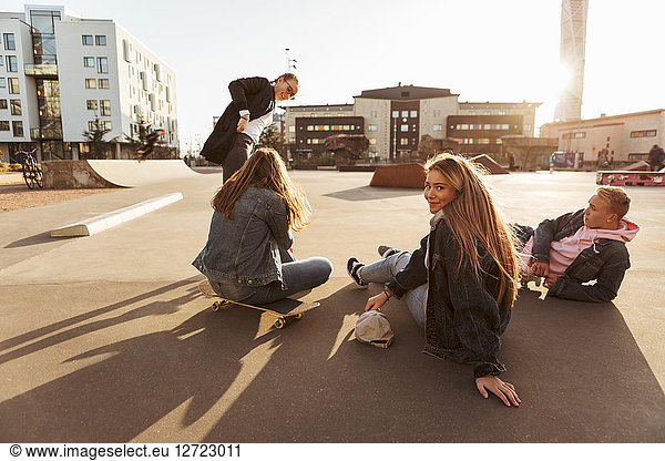 Portrait of smiling teenage girl hanging out with friends at skateboard park during sunny day