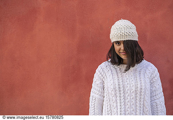Portrait of smiling teenage girl in fornt of red wall wearing white knitwear