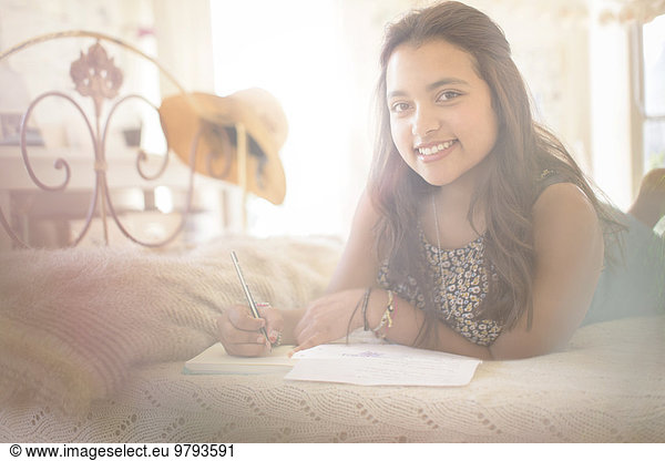 Portrait of smiling teenage girl lying on bed in bedroom