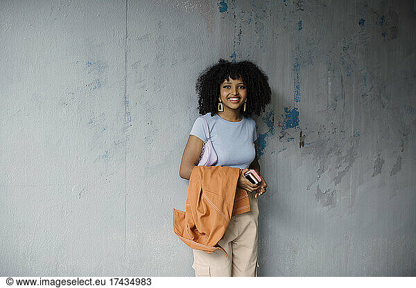 Portrait of smiling teenage girl standing against gray wall