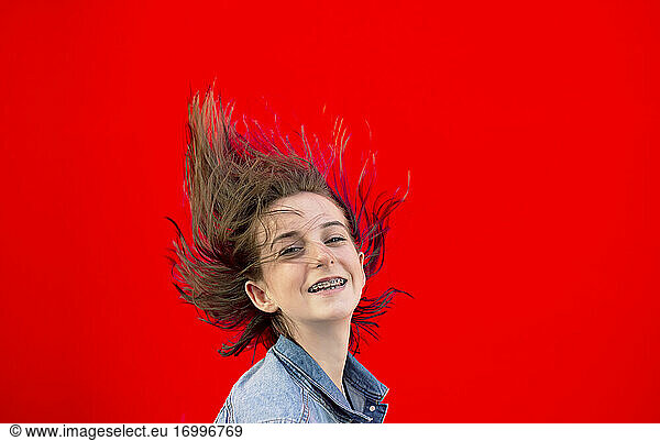 Portrait of smiling teenage girl with braces and blowing hair against red background