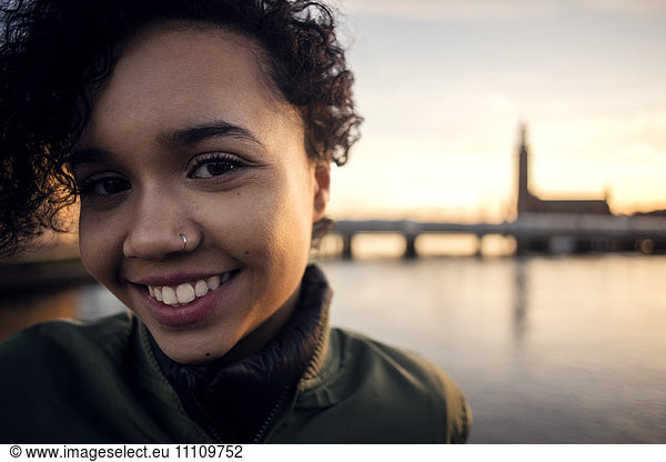 Portrait of smiling teenage girl with curly short hair standing against canal in city