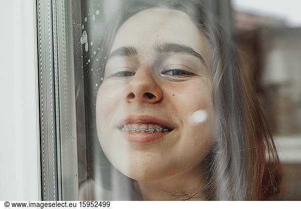 Portrait of smiling teenage girl with dental brace looking out of window
