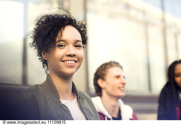 Portrait of smiling teenage girl with short curly hair standing with friends in city