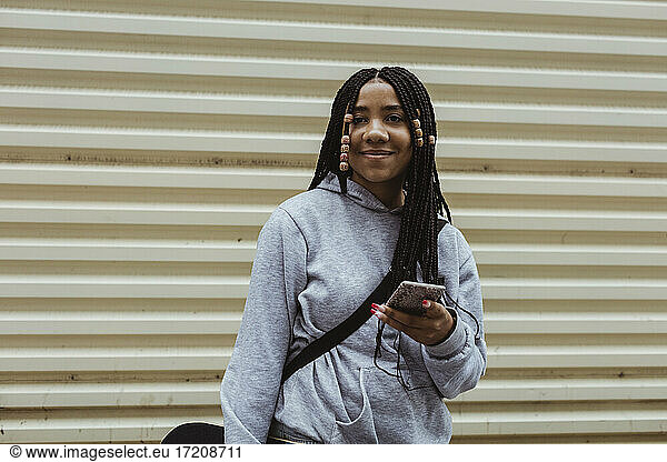 Portrait of smiling teenage girl with smart phone against wall