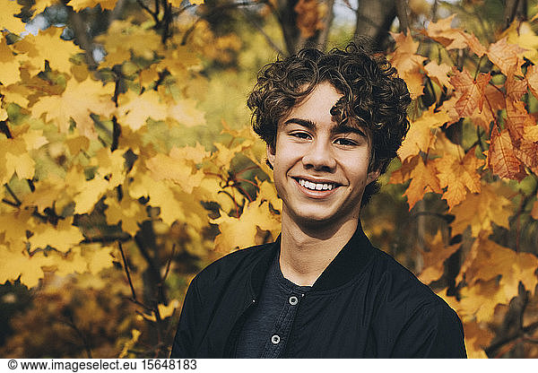 Portrait of smiling teenager with curly hair at park in autumn