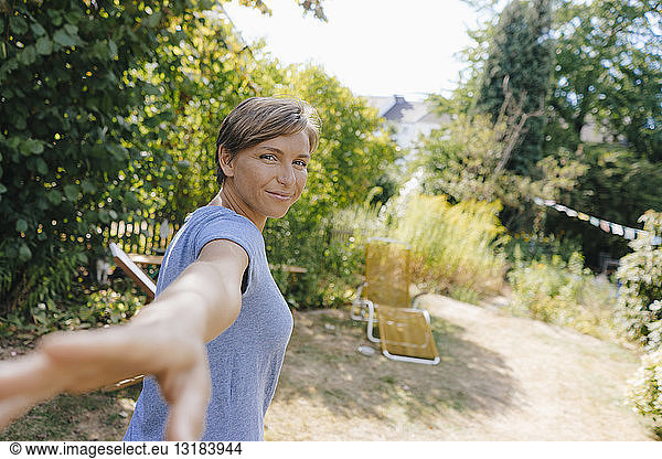 Portrait of smiling woman in garden reaching out