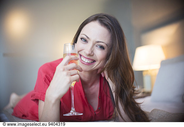 Portrait of smiling woman lying on bed with champagne flute