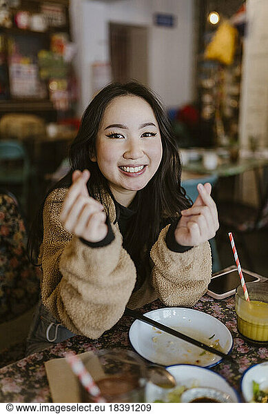 Portrait of smiling woman making heart shape with fingers at restaurant