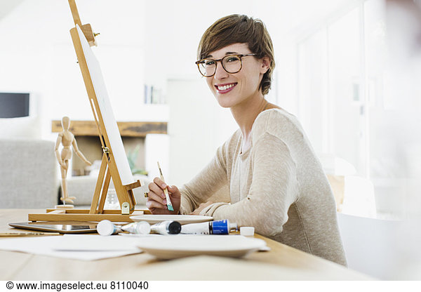 Portrait of smiling woman painting at easel on table
