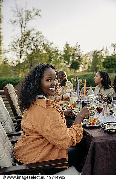 Portrait of smiling woman sitting at dining table during party in back yard