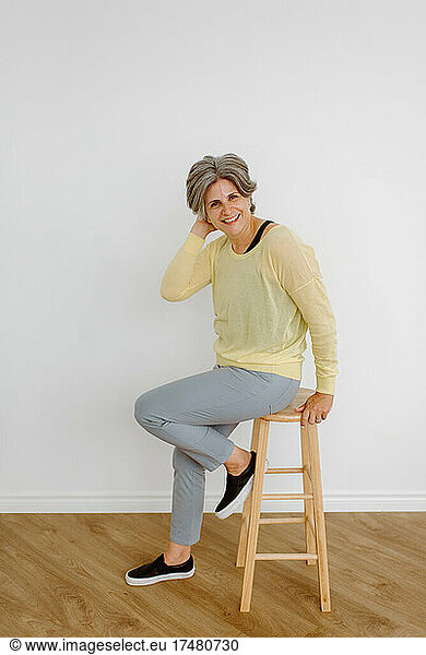 Portrait of smiling woman sitting on stool at home