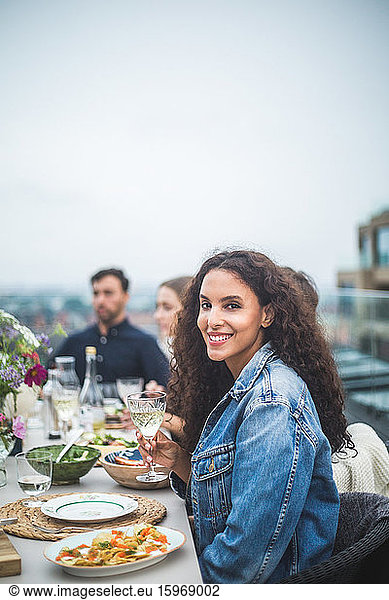 Portrait of smiling woman sitting with friends during social gathering on rooftop