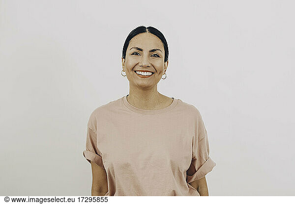 Portrait of smiling woman wearing peach color T-shirt against white background
