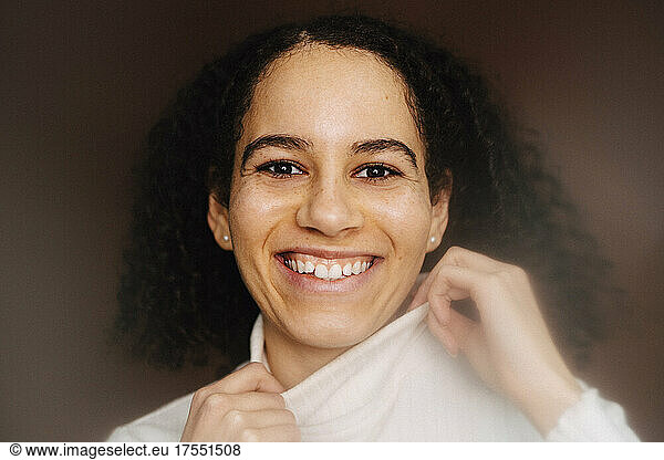 Portrait of smiling woman wearing turtleneck against brown background