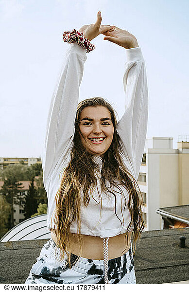 Portrait of smiling woman with arms raised practicing yoga on rooftop