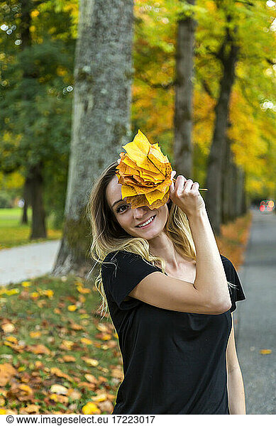 Portrait of smiling woman with bunch of autumn leaves on avenue