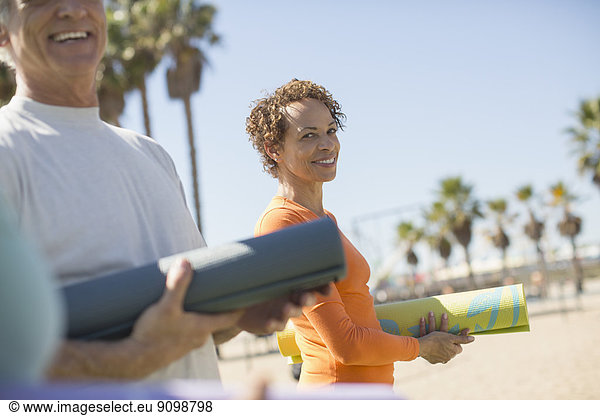 Portrait of smiling woman with yoga mat at beach