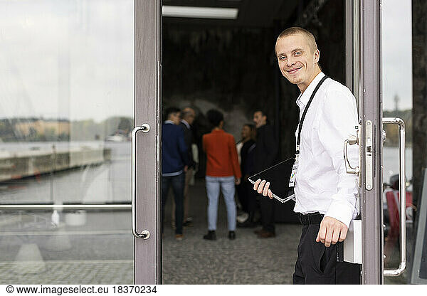 Portrait of smiling young businessman standing at doorway of convention center