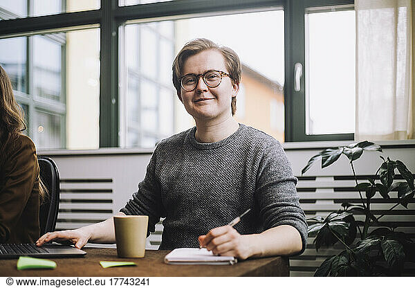 Portrait of smiling young businessman wearing eyeglasses sitting with diary at conference table