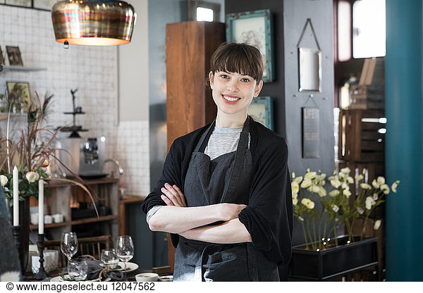 Portrait of smiling young female owner standing with arms crossed at store