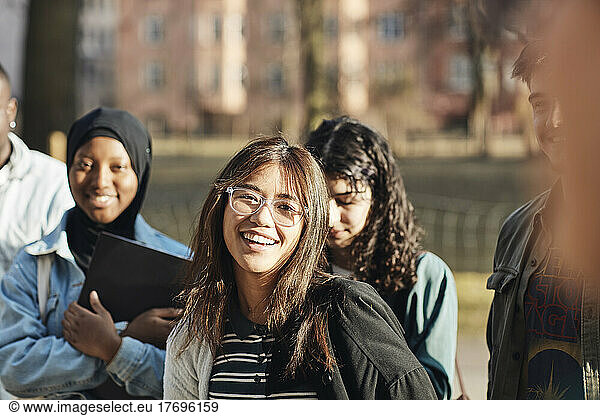 Portrait of smiling young female student with friends at university campus on sunny day