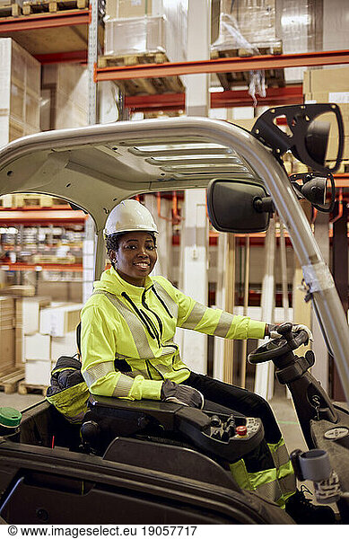 Portrait of smiling young female worker driving forklift in industry