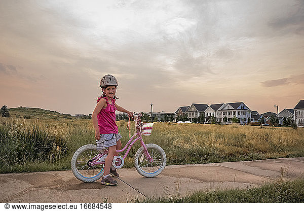 portrait of smiling young girl sitting on her bike in a park at sunset