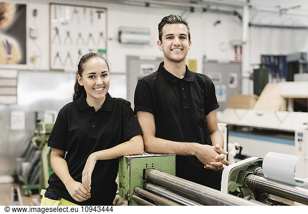 Portrait of smiling young high school students standing by machinery in workshop