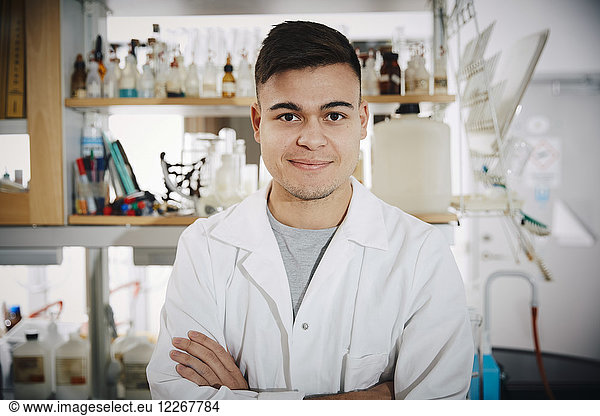 Portrait of smiling young male chemistry student standing with arms crossed in college laboratory