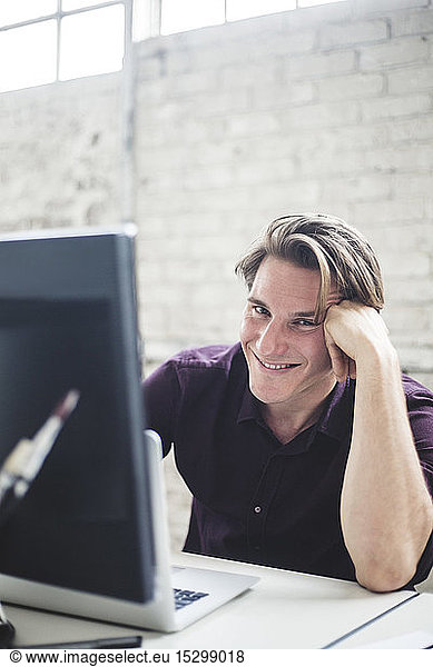 Portrait of smiling young male programmer coding at desk in office