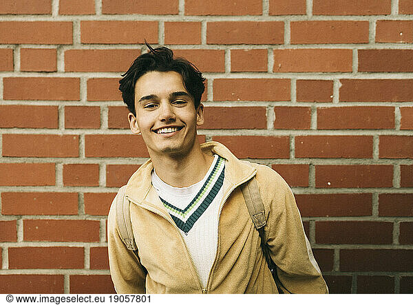 Portrait of smiling young man against brick wall