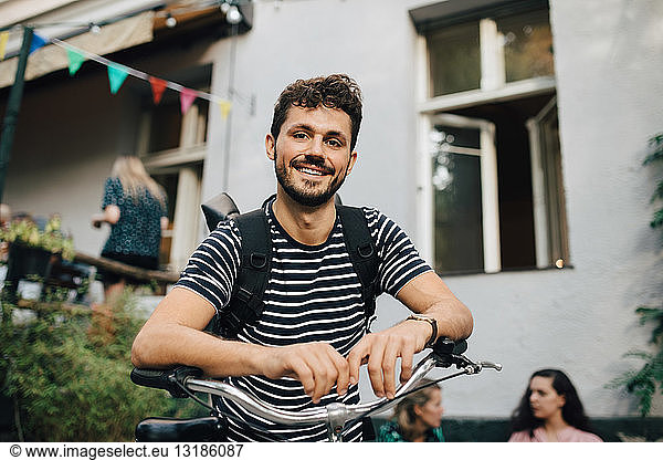 Portrait of smiling young man leaning on bicycle in backyard