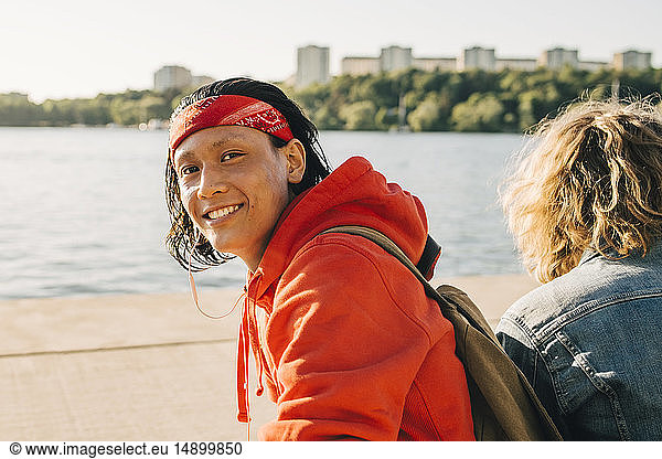 Portrait of smiling young man sitting by friend on promenade during sunny day