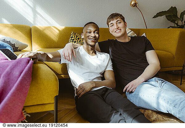 Portrait of smiling young man sitting with arm around friend at home