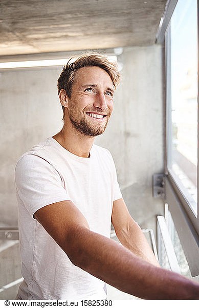 Portrait of smiling young man wearing white t-shirt looking out of window