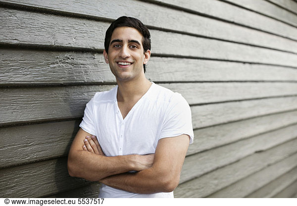 Portrait of smiling young man with arms crossed against wooden wall