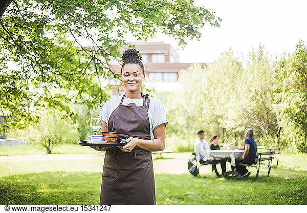 Portrait of smiling young waitress holding serving tray at outdoor cafe