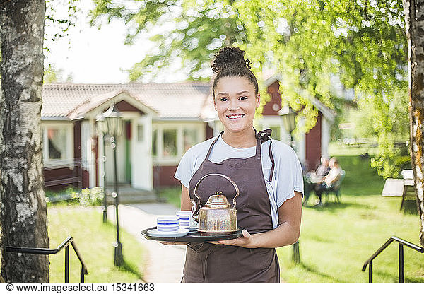 Portrait of smiling young waitress holding serving tray at restaurant