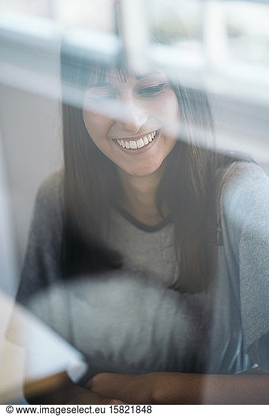 Portrait of smiling young woman behind windowpane