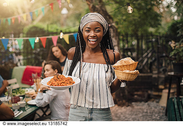 Portrait of smiling young woman carrying food while standing in backyard during garden party