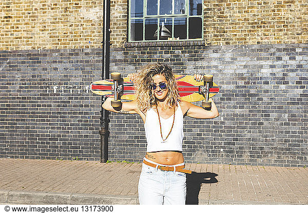 Portrait of smiling young woman carrying skateboard in the city