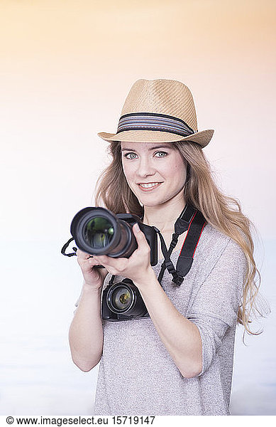 Portrait of smiling young woman comparing two different cameras